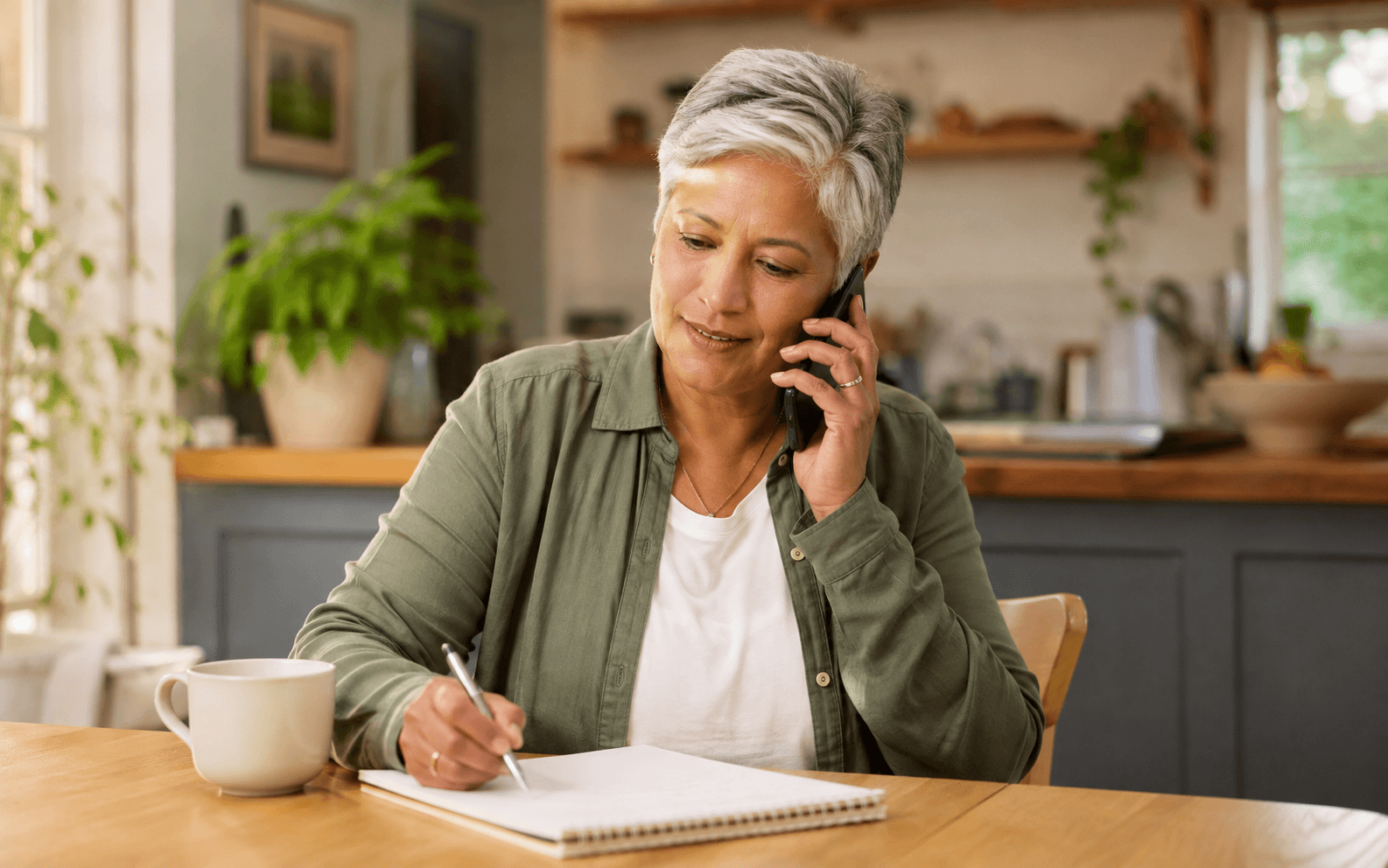 Older person on the phone with a notepad, making notes — in control of the conversation